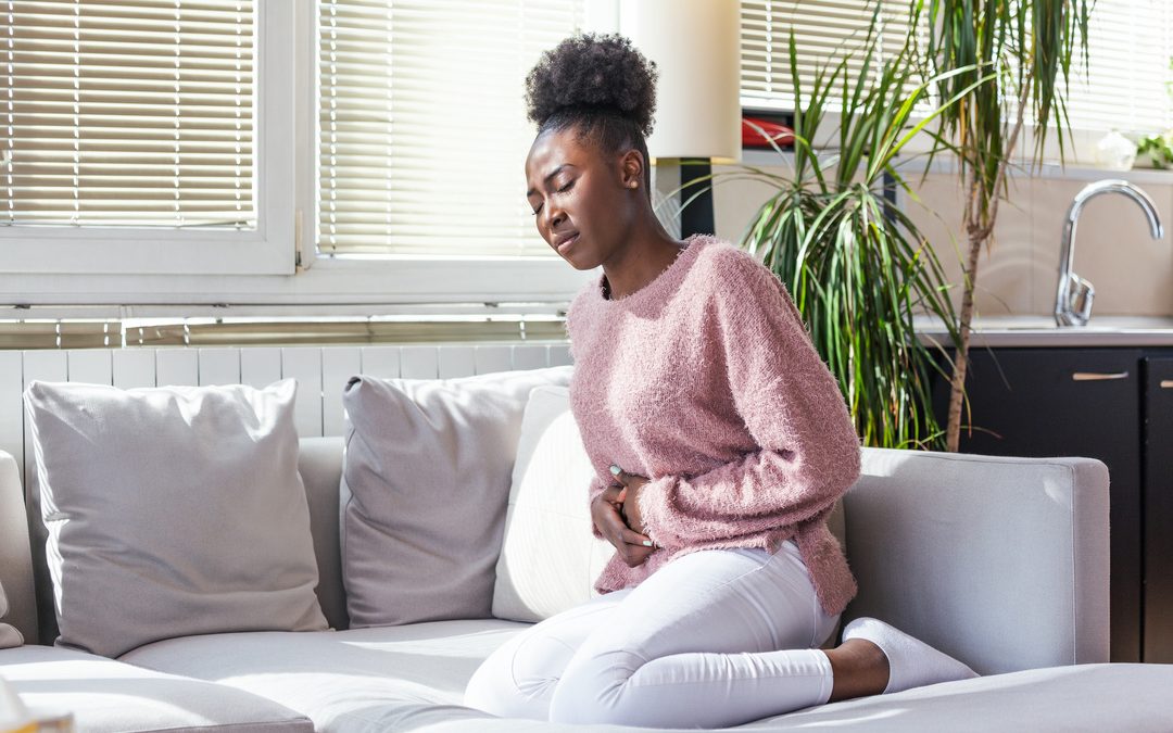 O que é gastrite - mulher de origem africana com a mão no estômago indicando dor