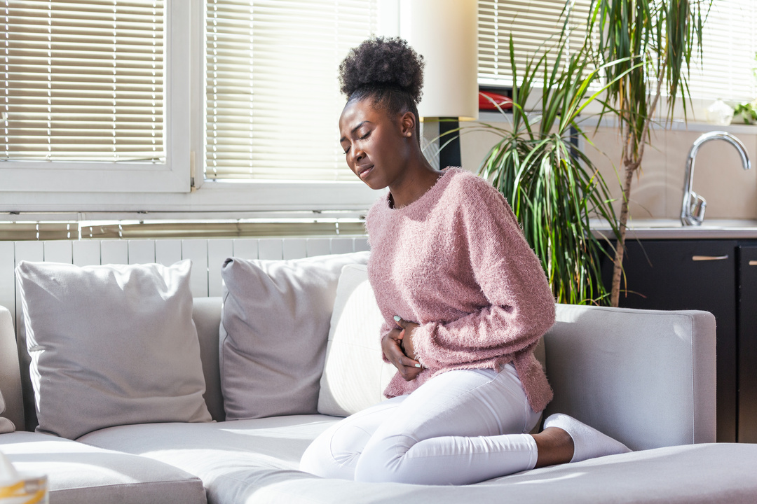 O que é gastrite - mulher de origem africana com a mão no estômago indicando dor