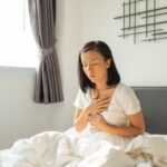 Autocuidados para refluxo gastroesofágico​: mulher na cama sentindo refluxo