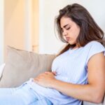 Intolerância à lactose inflama o intestino​: mulher no sofá com dor no abdômen.