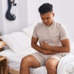 Obstrução intestinal é grave: homem sentado na cama com dor abdominal.