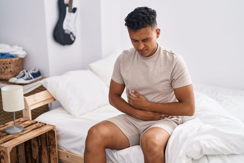 Obstrução intestinal é grave: homem sentado na cama com dor abdominal.