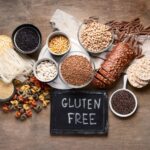 dieta sem glúten e sem lactose​: mesa com diversos alimentos em grãos e massas, com placa dizendo “gluten free”